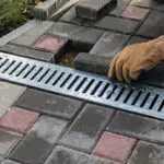 Worker installs metal drainage grate on patterned pavement.